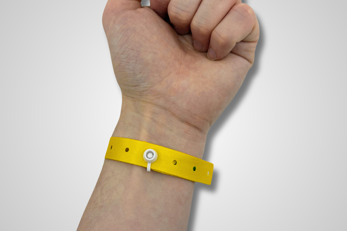 A button lock on a yellow festival wristband applied on to a wrist.